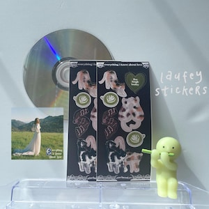 Puede incluir: Dos hojas de pegatinas con ilustraciones de gatos, tazas de café y el texto "everything i know about love" y "live laugh laufey".