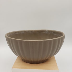 May include: A brown ceramic bowl with a fluted design. The bowl is sitting on a wooden surface.