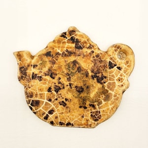 May include: A ceramic teapot with a crackled glaze in shades of brown and beige. The teapot features a detailed design of a bird or animal with intricate patterns.