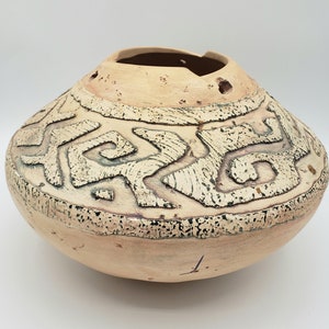 May include: A beige ceramic pot with a geometric pattern in black and white. The pot has a wide, rounded base and a slightly flared rim.