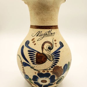 May include: A ceramic vase with a scalloped rim, painted in brown, blue, and white with a bird and floral designs. The vase is inscribed with the word "Mazatlan".
