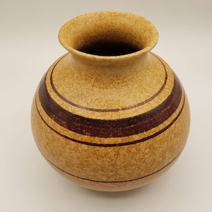 May include: A brown ceramic vase with a speckled glaze and brown stripes. The vase has a round body and a wide opening.