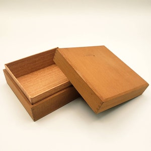 May include: A wooden box with a lid, the lid is open and the box is empty. The box is made of light brown wood and has a smooth finish.