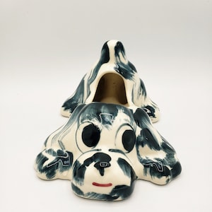 May include: A ceramic dog figurine with black and white paint, featuring a large open mouth and large eyes. The figurine is designed to be a planter or a decorative piece.