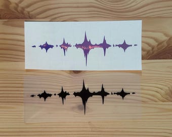 May include: Two stickers on a wooden surface. The top sticker is white with a purple and pink starburst design. The bottom sticker is transparent with a black starburst design. The stickers are likely for decoration.