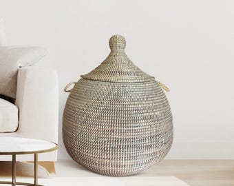 May include: A large, woven storage basket with a lid. The basket is a mix of neutral colours, with a rounded body and a conical lid. It has two small handles and is suitable for home decor.