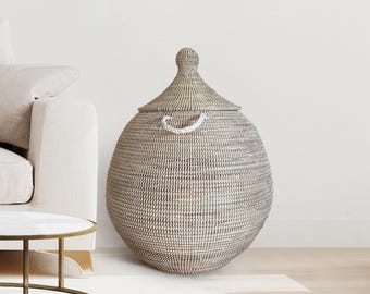 May include: A large, round, white and grey woven basket with a lid and a rope handle. The basket is made of natural materials and has a traditional design.