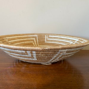 May include: A woven basket with a natural brown and white pattern. The basket is round and shallow, with a wide opening.