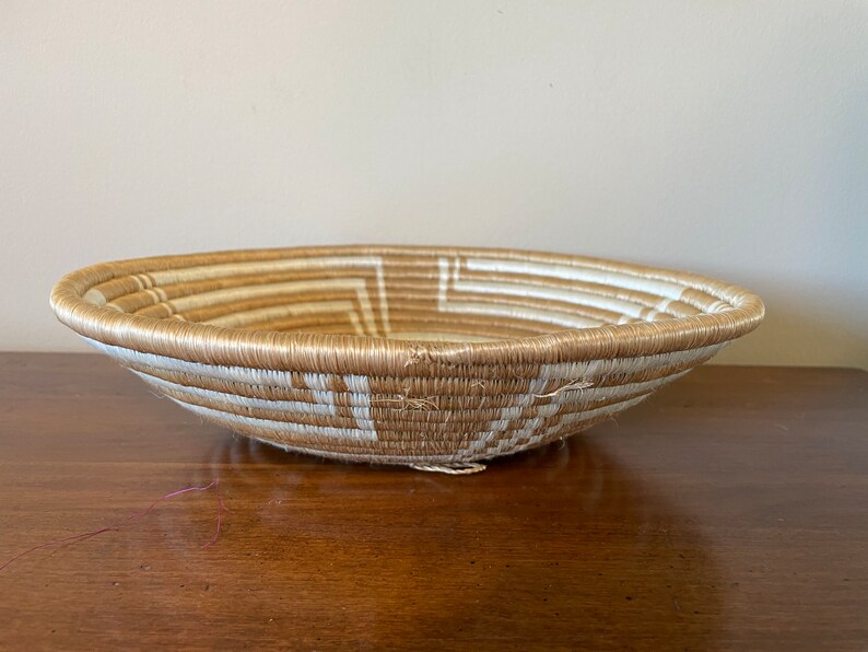 May include: A woven basket with a natural brown and white pattern. The basket is round and shallow, with a wide opening.