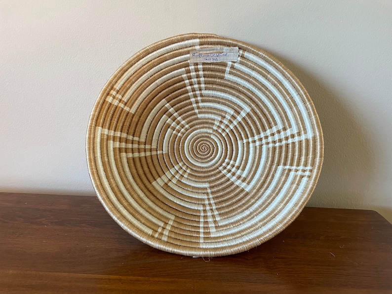 May include: A large, round woven basket with a white and tan pattern. The basket is made of natural materials and has a spiral design in the center.