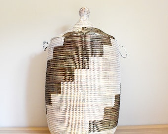 May include: A large, woven storage basket with a lid. The basket is made of natural fibres and has a geometric pattern of brown and white squares.