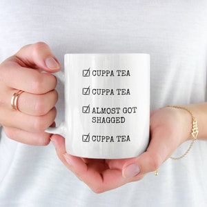 May include: White ceramic mug with a black tick and the text "Cuppa Tea" repeated three times. The fourth tick has the text "Almost Got Shagged"
