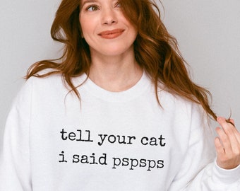 Può includere: Felpa bianca con la scritta "tell your cat i said pspsps" stampata sul davanti.
