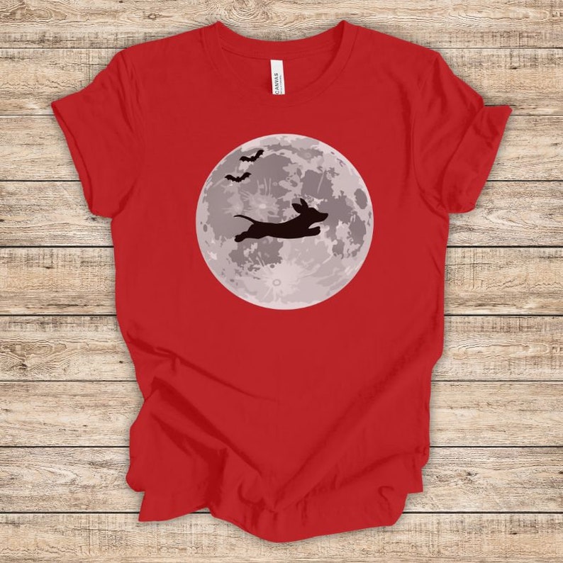 May include: Red t-shirt with a black silhouette of a dachshund jumping in front of a full moon with bats flying above.