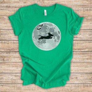 May include: A green t-shirt with a black silhouette of a dachshund jumping in front of a full moon with bats flying above.