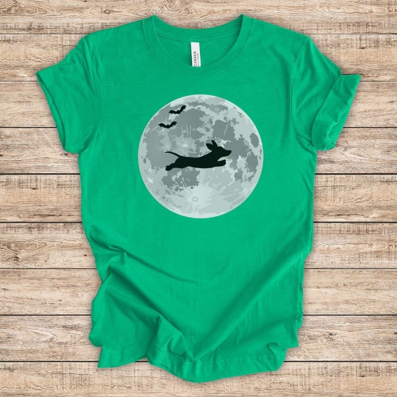 May include: A green t-shirt with a black silhouette of a dachshund jumping in front of a full moon with bats flying above.