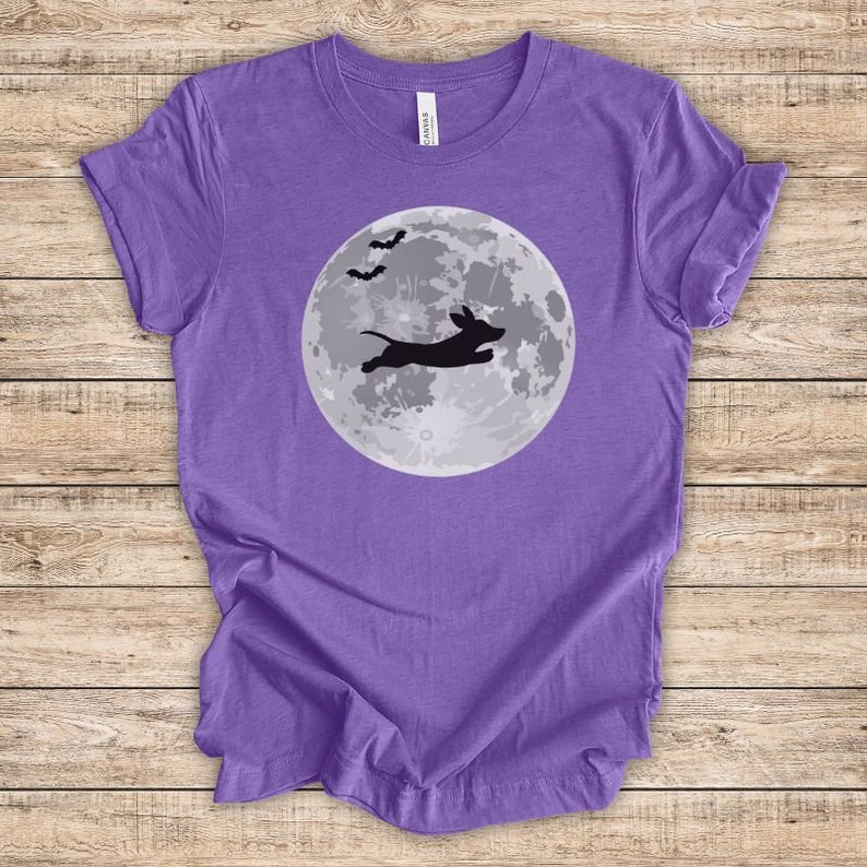 May include: Purple t-shirt with a black silhouette of a dachshund jumping in front of a full moon with bats flying above.
