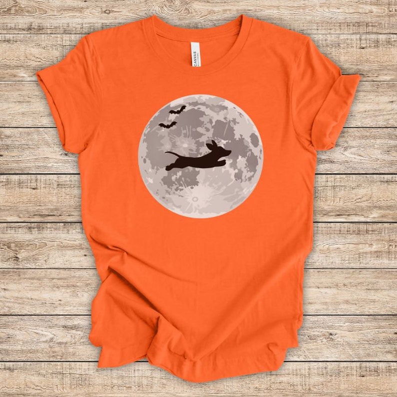 May include: Orange t-shirt with a silhouette of a dachshund jumping in front of a full moon with bats flying above.
