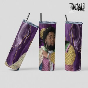 Può includere: Un bicchiere viola e oro con il viso di un uomo. L'uomo indossa una camicia a motivi rosa, verde e giallo e una catena d'oro intorno al collo. Il bicchiere è decorato con un motivo di glitter dorato.