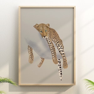 May include: A framed art print showing a stylized leopard with a spotted coat and blue eyes. The leopard is in a relaxed pose, draped over a soft, grey shape. The artwork is set against a neutral background, and framed in a light wood.