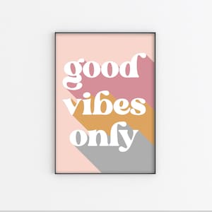 Op de afbeelding: Een ingelijst print met een roze, oranje en grijze achtergrond. De tekst "good vibes only" is in witte vetgedrukte letters geschreven.