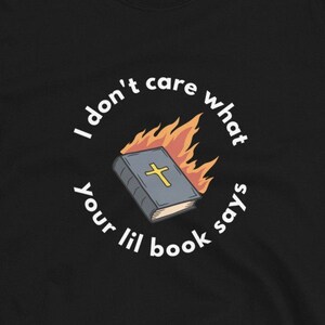 May include: Black t-shirt with a white circle graphic. The graphic features a burning book with a cross on the cover and the text "I don't care what your lil book says".