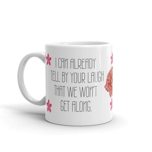 May include: White ceramic mug with the text "I CAN ALREADY TELL BY YOUR LAUGH THAT WE WON'T GET ALONG." The mug features pink flower illustrations and a floral design. The mug has a white handle.