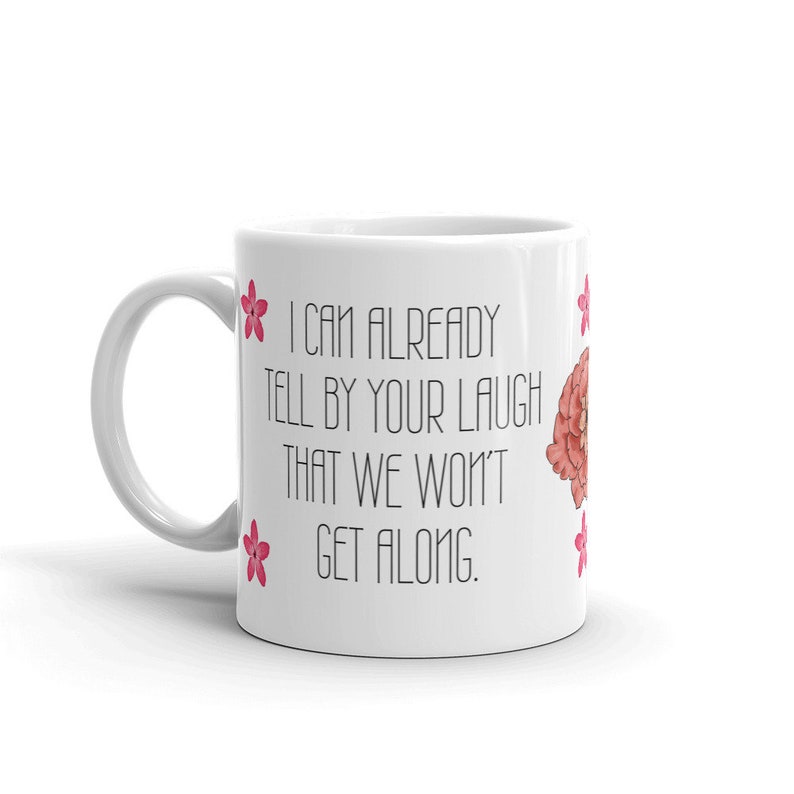 May include: White ceramic mug with the text "I CAN ALREADY TELL BY YOUR LAUGH THAT WE WON'T GET ALONG." The mug features pink flower illustrations and a floral design. The mug has a white handle.