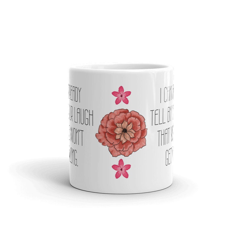 May include: White ceramic mug with a large, watercolor-style pink flower and two smaller pink flowers. The mug has black text that reads, "Ready for a laugh? I won't be long. I can tell by that it's getting..."