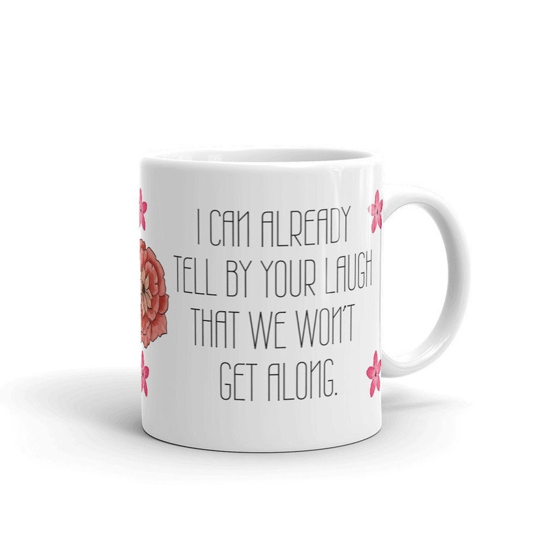 May include: White ceramic mug with a handle, featuring the text "I CAN ALREADY TELL BY YOUR LAUGH THAT WE WON'T GET ALONG." The mug is decorated with a red and pink floral design and pink flower accents.