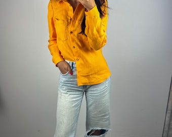 May include: A bright orange long-sleeved button-down shirt with a collar and a single chest pocket, paired with light-wash blue denim jeans featuring distressed knee cutouts and a wide-leg fit, worn with black open-toe sandals.
