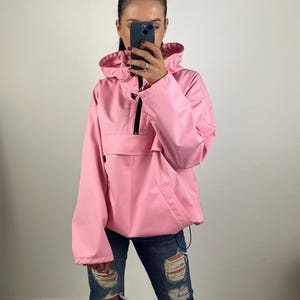 Può includere: Una giacca rosa con cappuccio, chiusura a zip e una grande tasca sul davanti. La giacca è realizzata in un materiale leggero e resistente all'acqua.