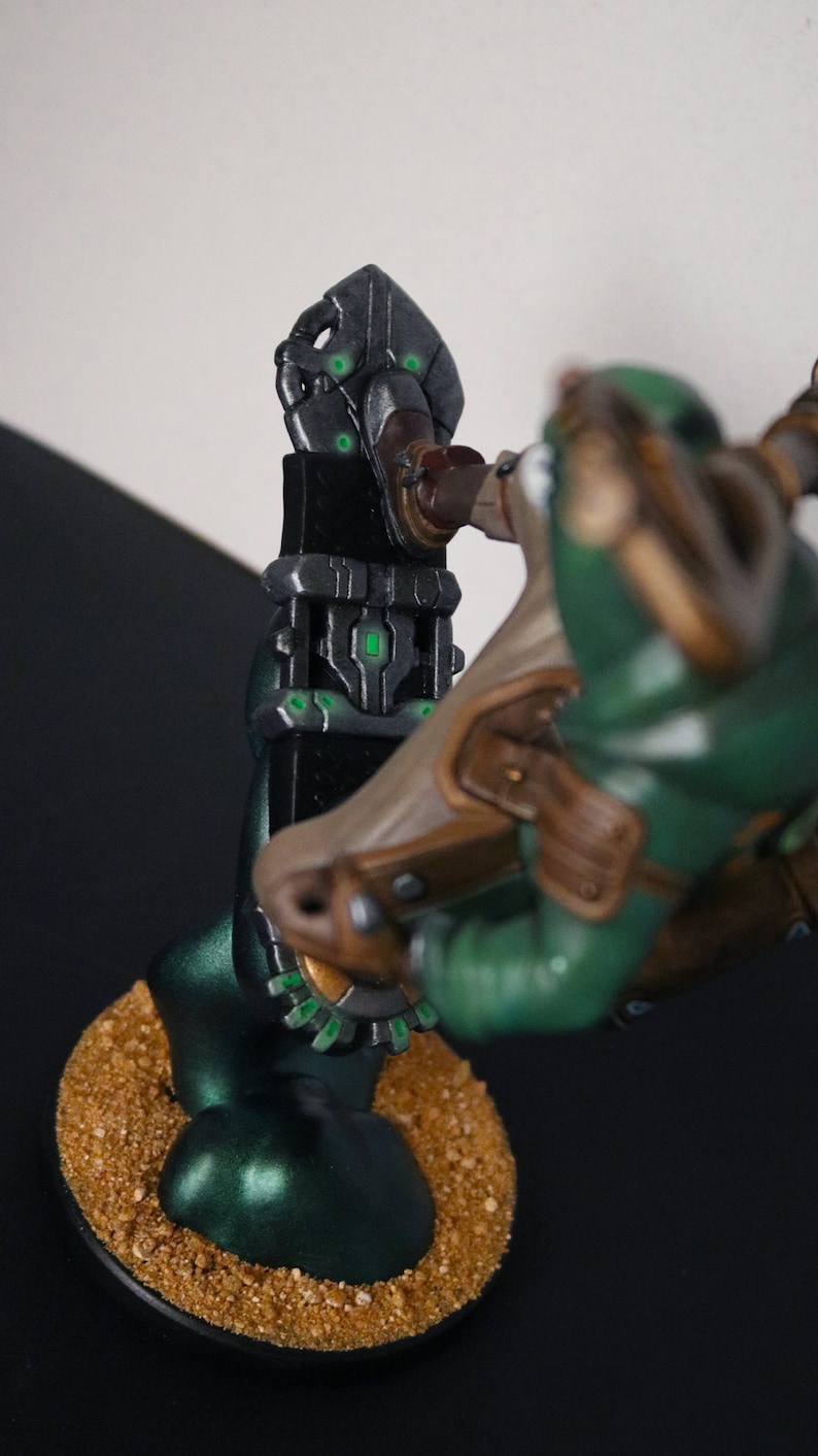 Pu&ograve; includere: Statuetta dettagliata di un personaggio di fantascienza con armatura verde e marrone, in posa vicino a una struttura scura e futuristica. La base &egrave; strutturata con un aspetto sabbioso e la struttura ha accenti verdi luminosi.
