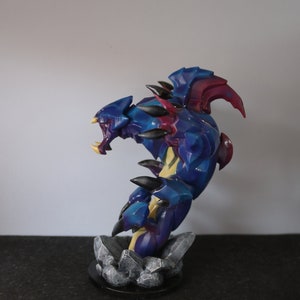 May include: A detailed figurine of a fantasy creature with a blue and purple color scheme. The figure has sharp claws, teeth, and spikes. It is posed on a rocky base, with a black circular base. The figurine is approximately 6 inches tall.