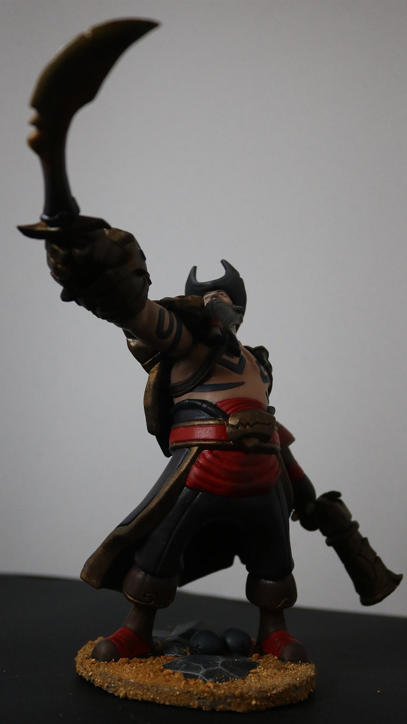 May include: A detailed figurine of a pirate, holding a curved blade and a pistol. The figure wears a tricorn hat, a red sash, and black pants. The base is textured with sand and small rocks. The color palette includes gold, red, black, and tan.