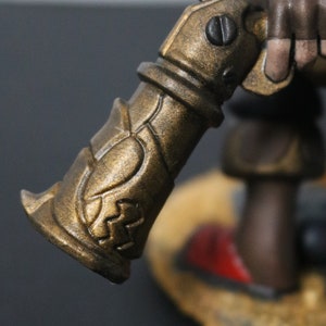May include: Close-up of a bronze-colored, ornate weapon with intricate detailing. The weapon has a cylindrical body with decorative patterns and a handle. The overall design suggests a fantasy or historical theme.