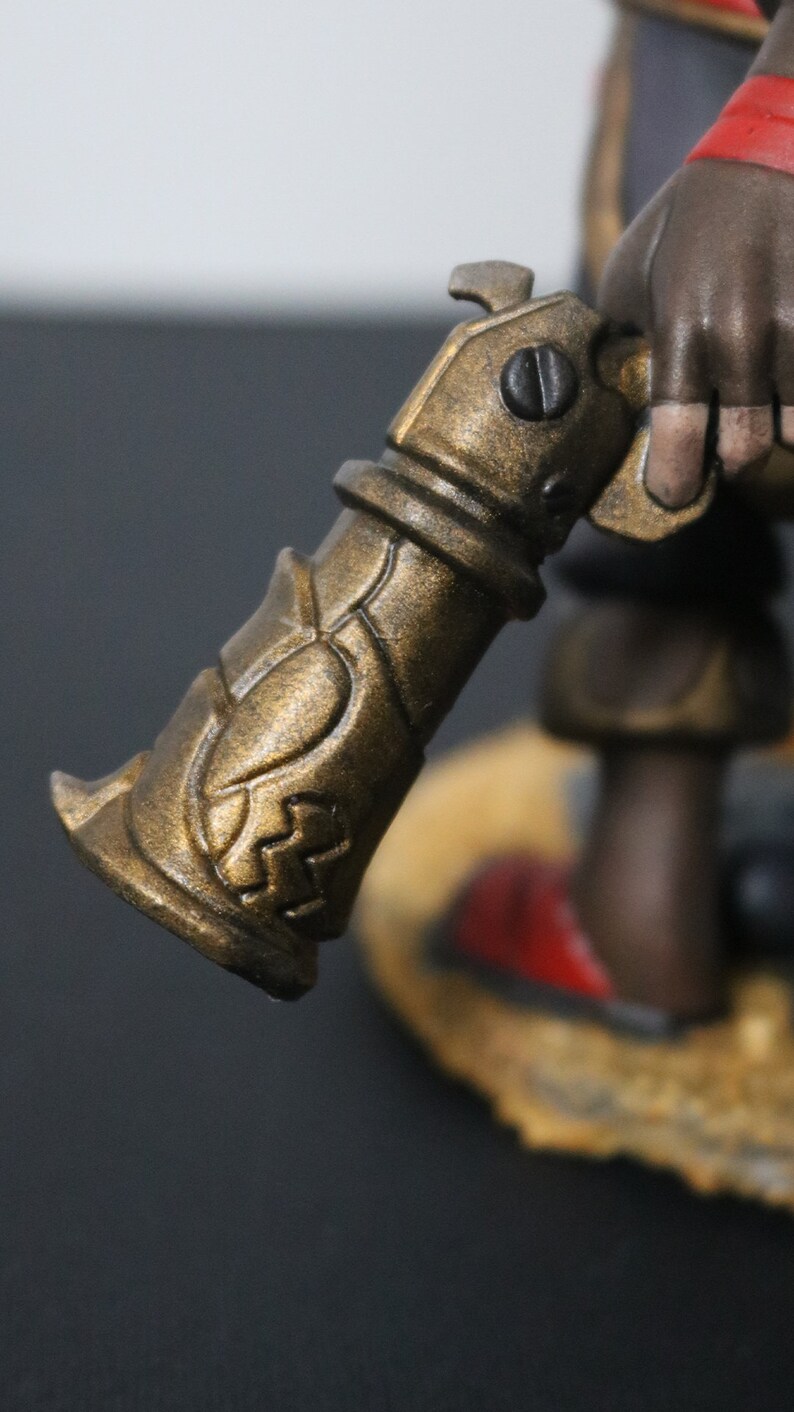 May include: Close-up of a bronze-colored, ornate weapon with intricate detailing. The weapon has a cylindrical body with decorative patterns and a handle. The overall design suggests a fantasy or historical theme.