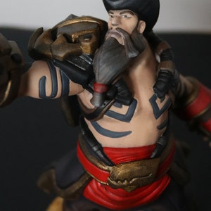May include: A detailed figurine of a muscular character with a beard and a black hat. The figure is painted with a combination of colors, including red, gold, black, and tan. The character has tattoos and is posed in a dynamic stance.