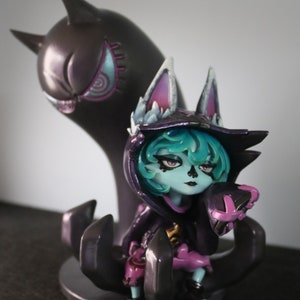 May include: A detailed figurine of a character with teal hair, wearing a black hooded outfit with purple accents. A dark purple ghost-like figure stands behind the character. The figurine is on a dark base.
