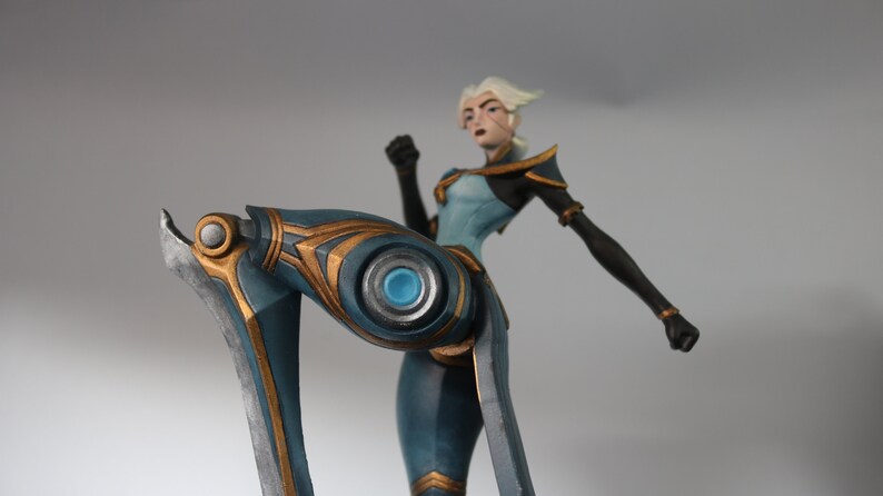 May include: A detailed figurine of a character in a dynamic pose. The figure is predominantly blue with gold accents, and the design suggests a futuristic or fantasy theme. The character has white hair and is in a fighting stance.
