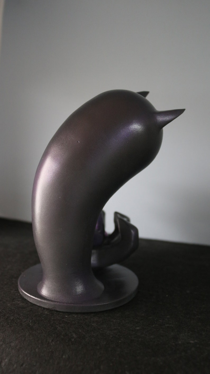 May include: A dark grey, abstract sculpture with a curved body and two small, pointed horns. The sculpture sits on a circular base and has a smooth, metallic finish. The object is likely a decorative piece or art object.