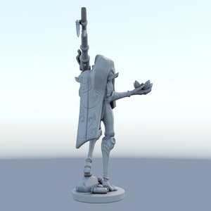 May include: A gray figurine of a character holding a weapon and a lotus flower. The figure is wearing a cape with a decorative swirl design. The figurine is standing on a round base.