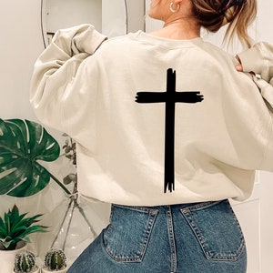 May include: A cream colored sweatshirt with a black brushstroke cross design on the back.