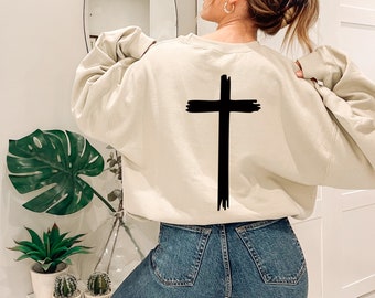 May include: A cream colored sweatshirt with a black brushstroke cross design on the back.