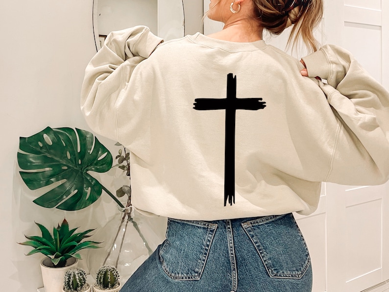May include: A cream colored sweatshirt with a black brushstroke cross design on the back.