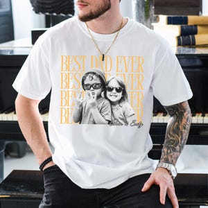 A man wearing a white t-shirt with a graphic design featuring two children and the text "BEST DAD EVER" printed on it.