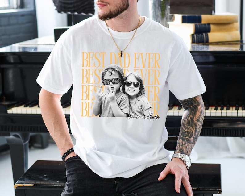 A man wearing a white t-shirt with a graphic design featuring two children and the text "BEST DAD EVER" printed on it.