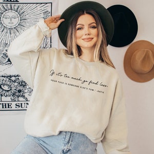May include: A light beige sweatshirt with the text "If it's too much, go find less. Your yuck is someone else's yum. -Katie" printed in black.