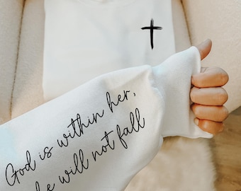 May include: White sweatshirt with a black cross on the front and the text "God is within her, she will not fall" on the sleeve.