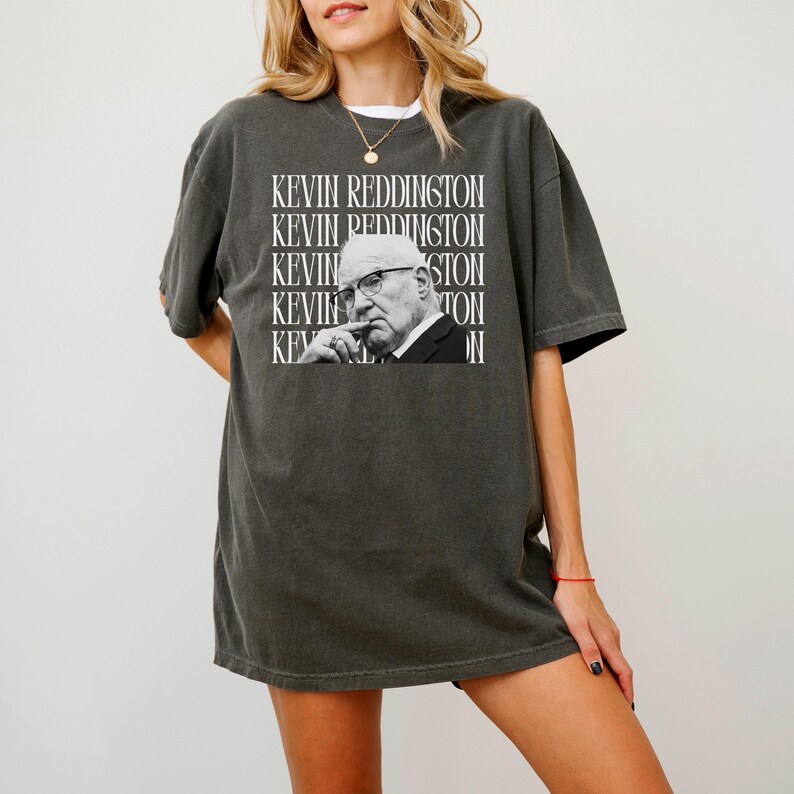 A woman wearing a gray t-shirt with a graphic of a man's face and the text "KEVIN REDDINGTON" repeated across the shirt.